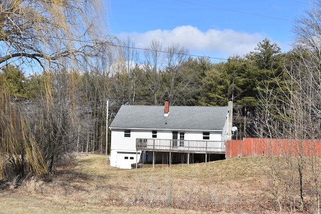 back of property with roof with shingles, a chimney, an attached garage, driveway, and a wooden deck