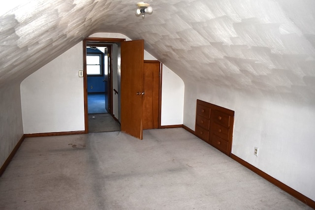 additional living space featuring vaulted ceiling, light colored carpet, and baseboards