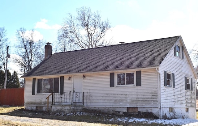 view of front facade featuring roof with shingles, a chimney, and fence