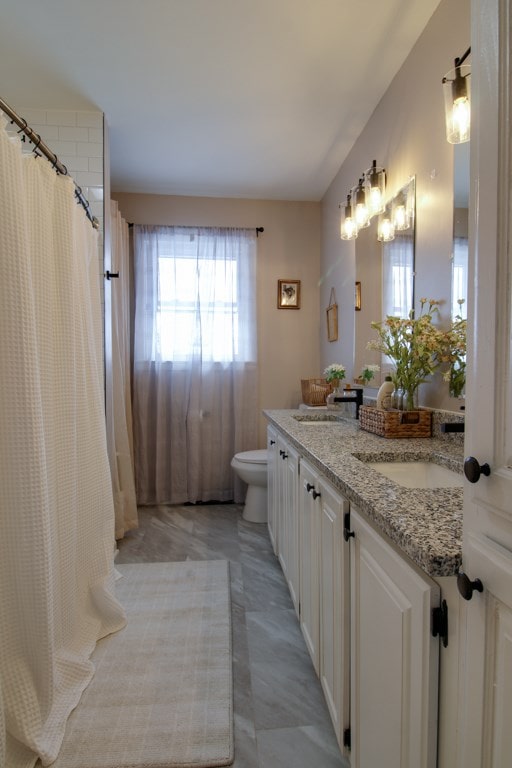 full bath with double vanity, curtained shower, a sink, and toilet