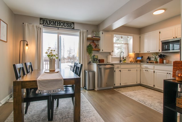 kitchen with stainless steel appliances, white cabinets, light wood finished floors, and tasteful backsplash