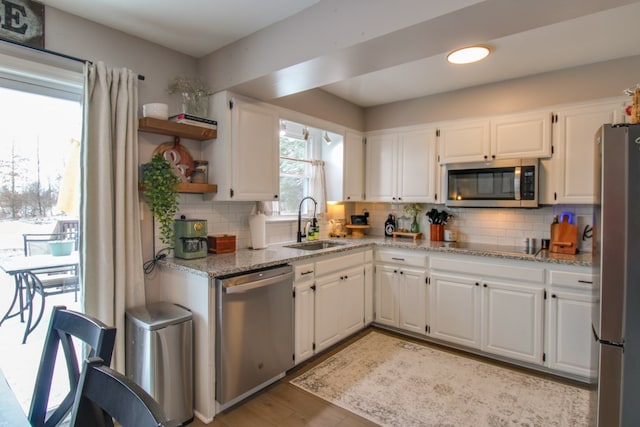 kitchen featuring a sink, white cabinetry, appliances with stainless steel finishes, light stone countertops, and tasteful backsplash
