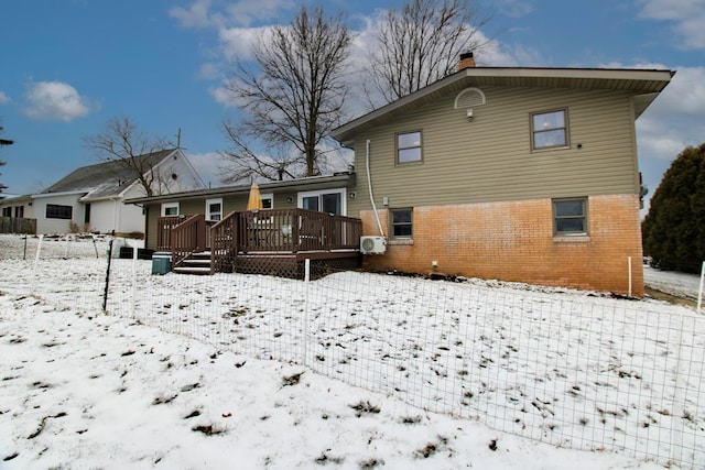 snow covered property with a chimney, a deck, and brick siding