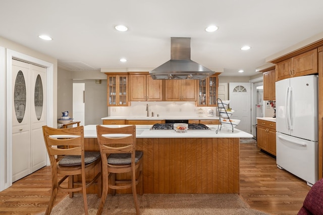 kitchen featuring stainless steel gas cooktop, brown cabinets, island exhaust hood, and freestanding refrigerator