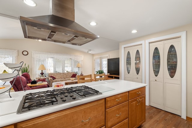 kitchen with wood finished floors, island range hood, light countertops, vaulted ceiling, and stainless steel gas cooktop