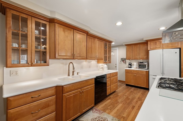 kitchen featuring light countertops, black dishwasher, freestanding refrigerator, wall chimney exhaust hood, and a sink