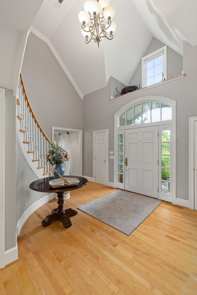 entrance foyer featuring high vaulted ceiling, baseboards, wood finished floors, stairway, and an inviting chandelier