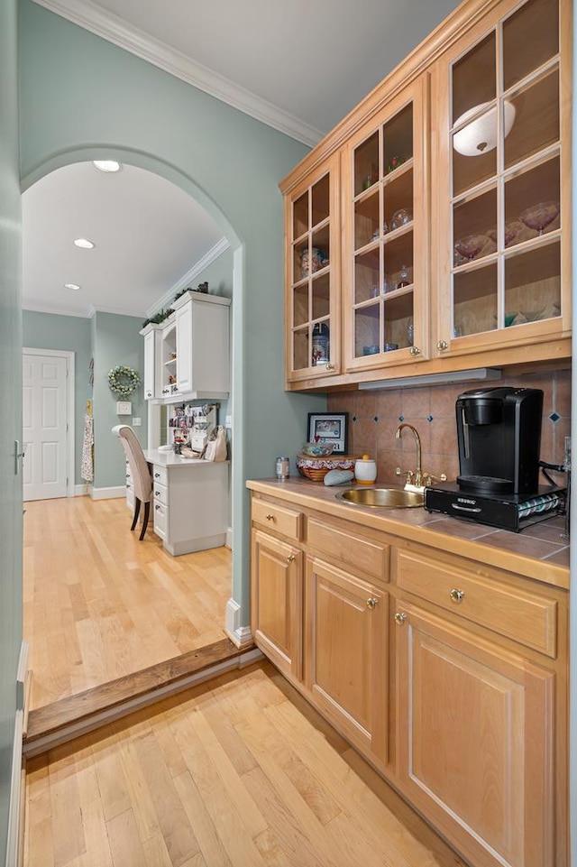 kitchen featuring light wood-style flooring, crown molding, arched walkways, a sink, and backsplash