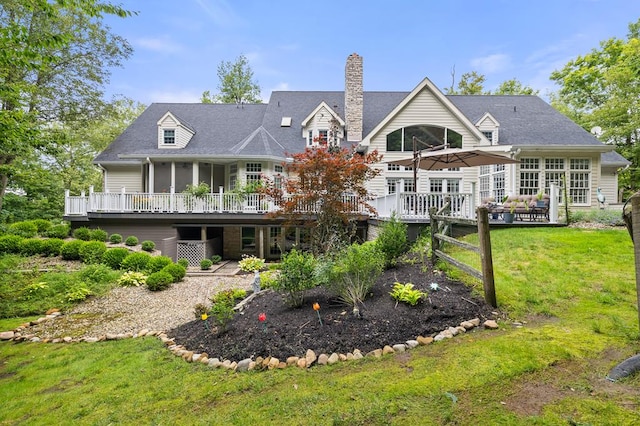 back of property with a chimney, a wooden deck, and a yard
