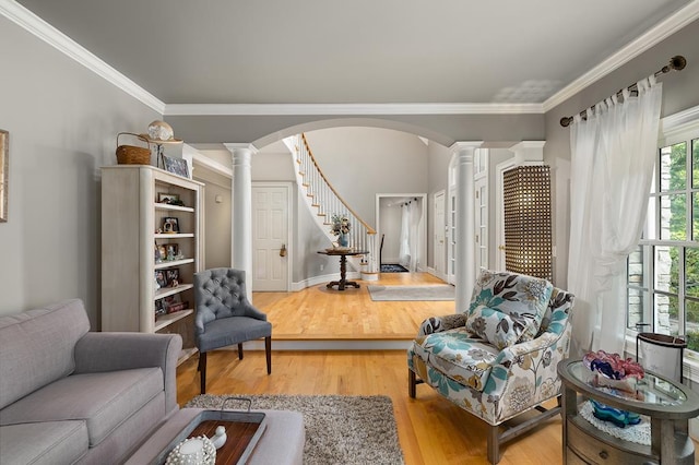 living area with arched walkways, crown molding, wood finished floors, and decorative columns