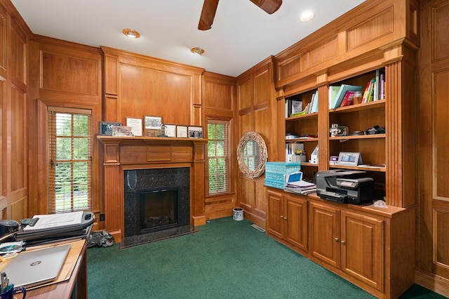 office featuring carpet floors, wooden walls, a premium fireplace, and ceiling fan