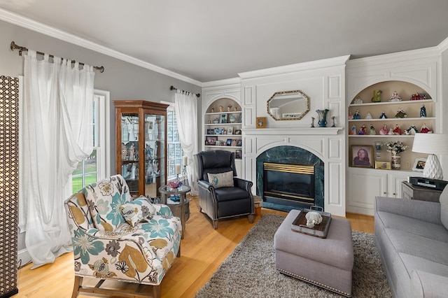 living room with a high end fireplace, crown molding, built in shelves, and light wood-type flooring