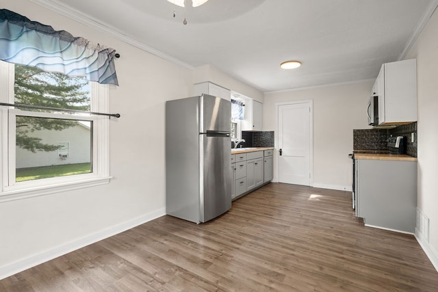 110 Hill St, Edison, OH 43320 - kitchen featuring appliances with stainless steel finishes, backsplash, ornamental molding, wood finished floors, and white cabinets