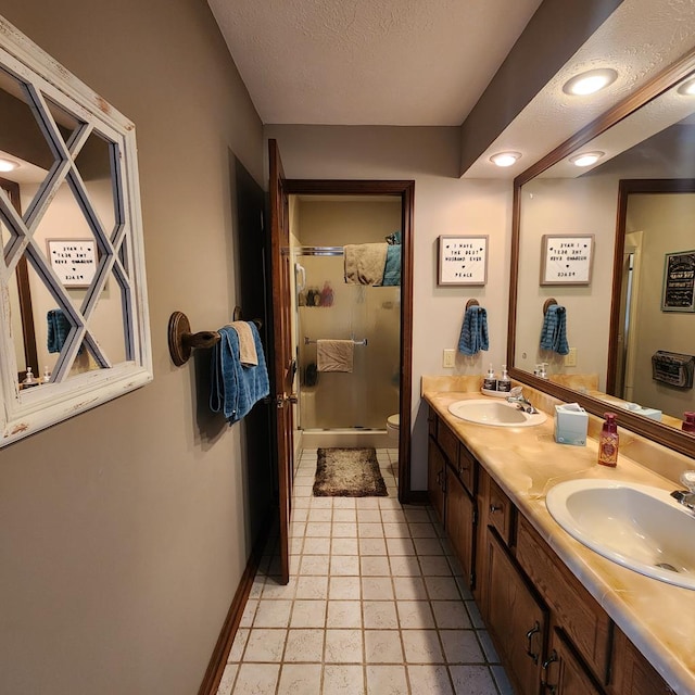 bathroom featuring a sink, a shower stall, a textured ceiling, and double vanity