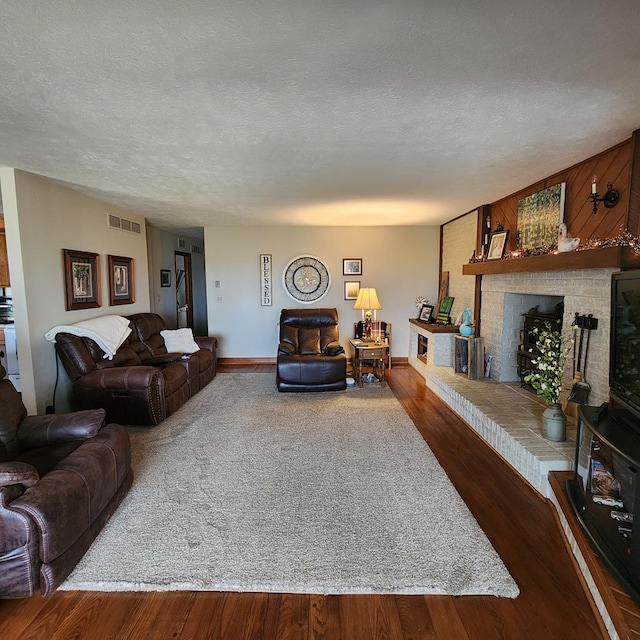 living area with a brick fireplace, visible vents, a textured ceiling, and wood finished floors