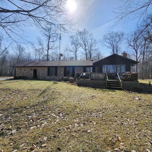 view of front of home featuring a front lawn, stone siding, a chimney, and a wooden deck