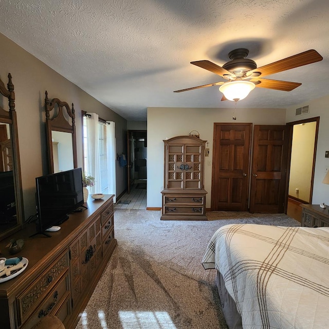 bedroom featuring a textured ceiling, carpet flooring, visible vents, a ceiling fan, and ensuite bath