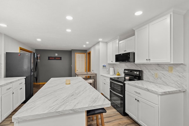 kitchen with decorative backsplash, white cabinetry, black appliances, and light wood-type flooring