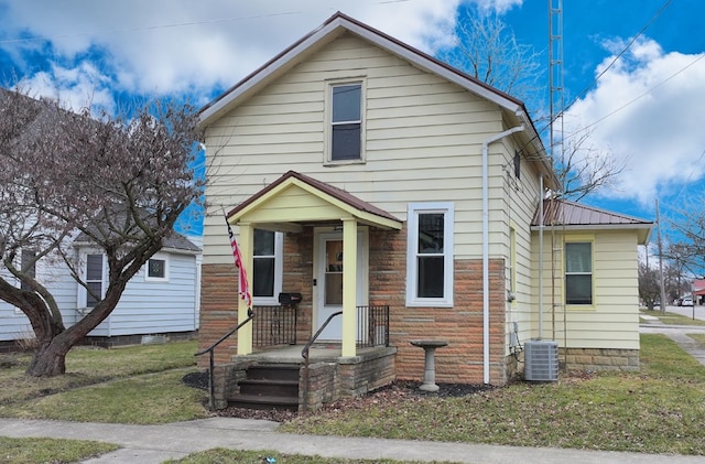 view of front of house with central air condition unit, metal roof, and a front lawn