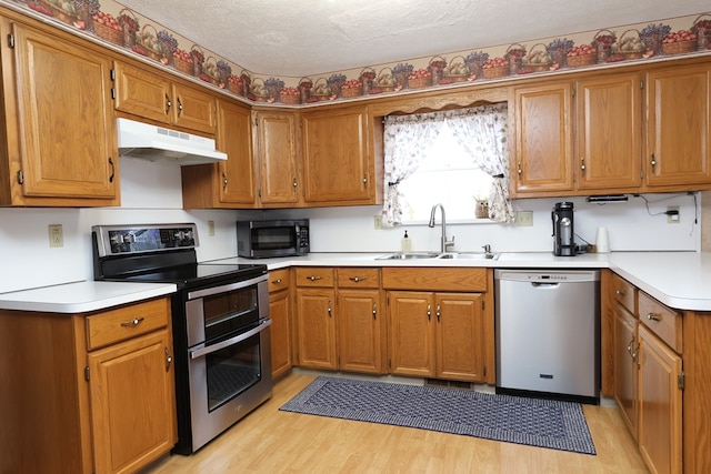 kitchen with appliances with stainless steel finishes, a textured ceiling, light hardwood / wood-style floors, and sink