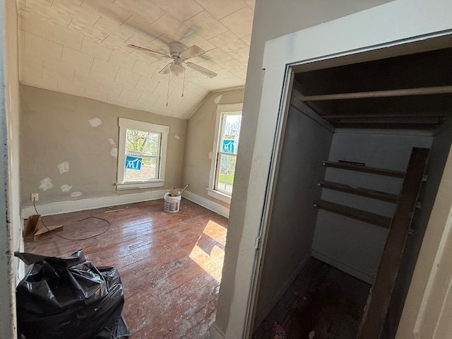 interior space with baseboards, ceiling fan, wood-type flooring, and vaulted ceiling