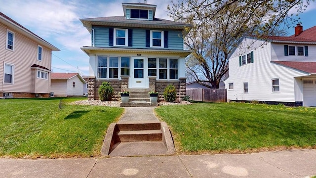 american foursquare style home with entry steps, stone siding, a front yard, and fence