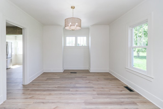 empty room featuring a chandelier, plenty of natural light, light wood finished floors, and visible vents
