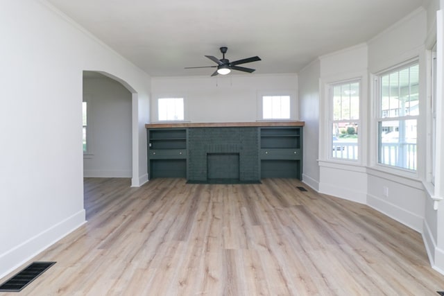 unfurnished living room with a ceiling fan, visible vents, arched walkways, light wood-type flooring, and baseboards
