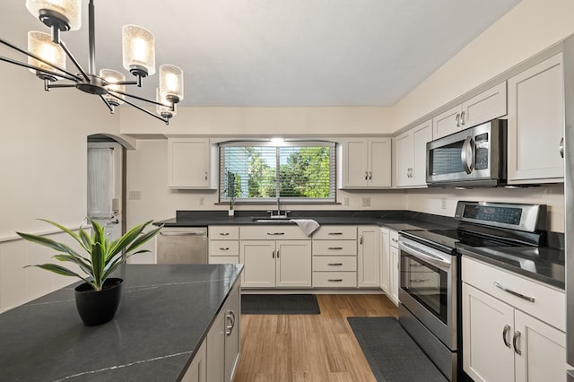 kitchen with an inviting chandelier, sink, hanging light fixtures, white cabinetry, and stainless steel appliances