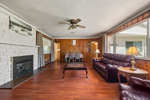 living room featuring ceiling fan, dark wood-type flooring, baseboard heating, crown molding, and a fireplace