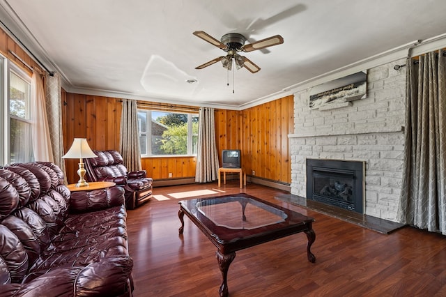 living room featuring ceiling fan, wood walls, a stone fireplace, and ornamental molding