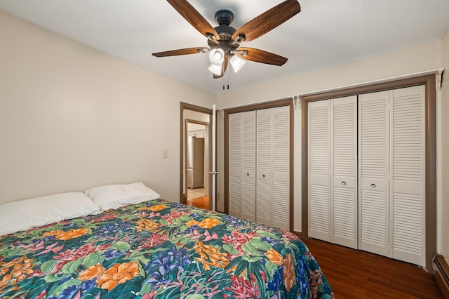 bedroom with ceiling fan, a baseboard radiator, dark hardwood / wood-style floors, stainless steel refrigerator, and multiple closets