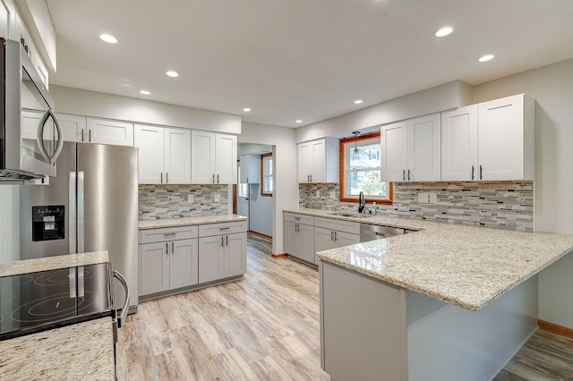 42 Kester Dr, Mount Vernon, OH 43050 - kitchen featuring appliances with stainless steel finishes, a sink, light wood finished floors, decorative backsplash, and a peninsula