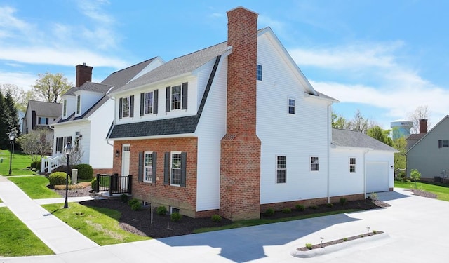 view of side of home featuring a garage, a chimney, concrete driveway, and roof with shingles