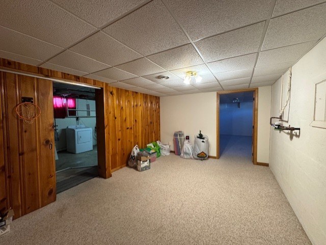 finished basement with wooden walls, washer / clothes dryer, a paneled ceiling, and carpet