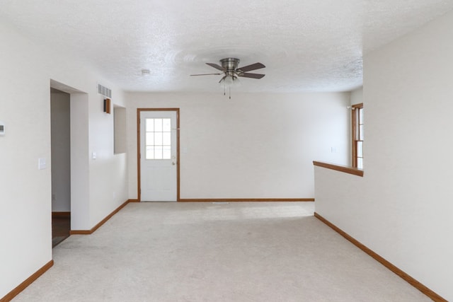 empty room featuring a textured ceiling, light colored carpet, and ceiling fan