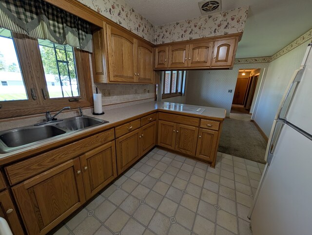 kitchen with brown cabinets, white appliances, wallpapered walls, and a sink