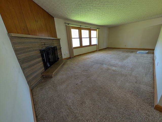 unfurnished living room with a textured ceiling, a fireplace with raised hearth, baseboards, and carpet floors