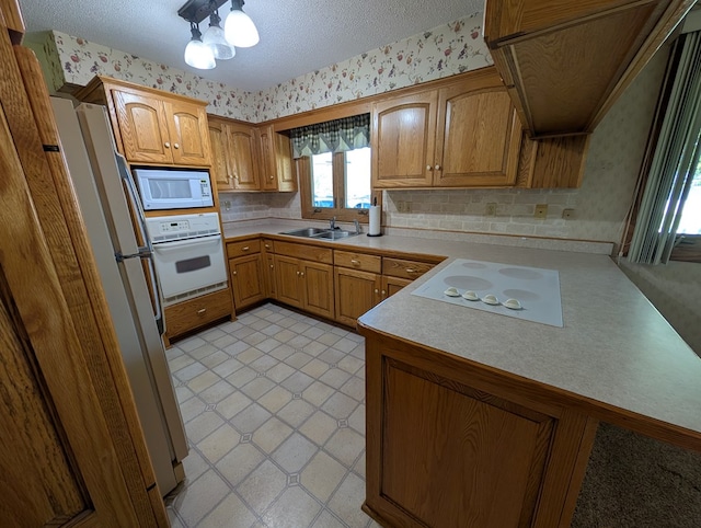 kitchen with wallpapered walls, white appliances, and a sink