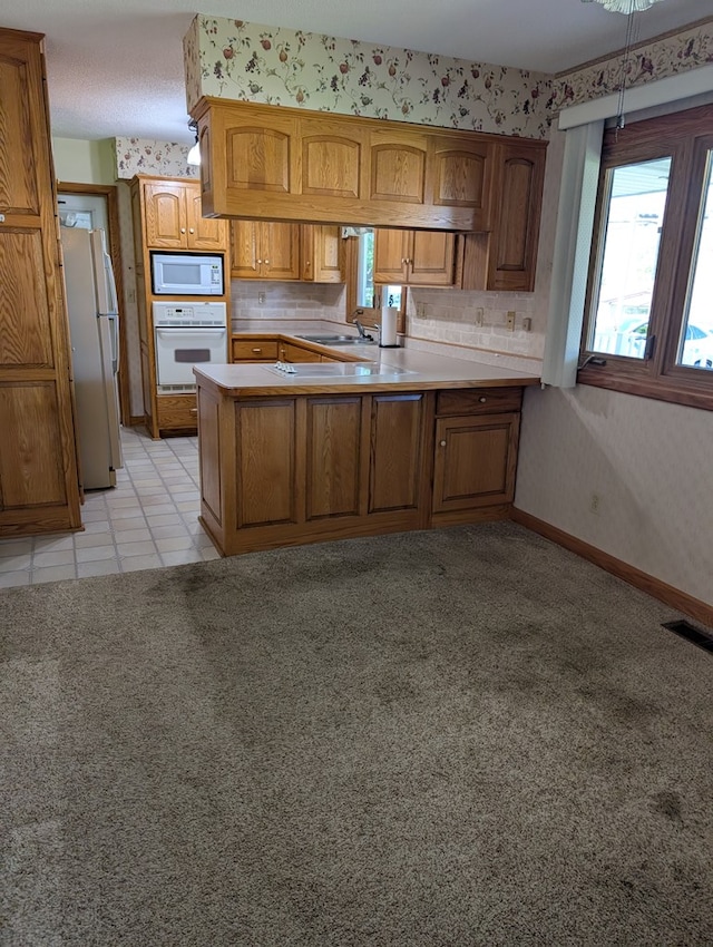 kitchen featuring white appliances, light countertops, brown cabinets, visible vents, and a peninsula
