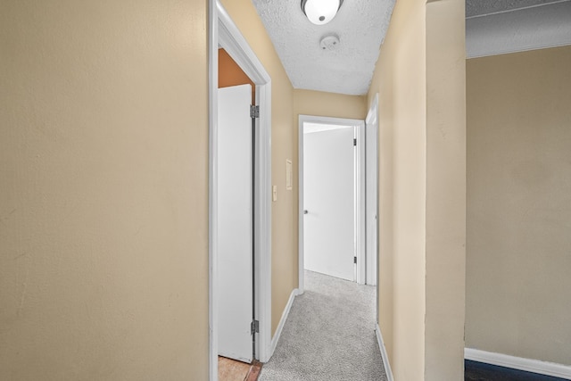 hall featuring carpet flooring, baseboards, and a textured ceiling