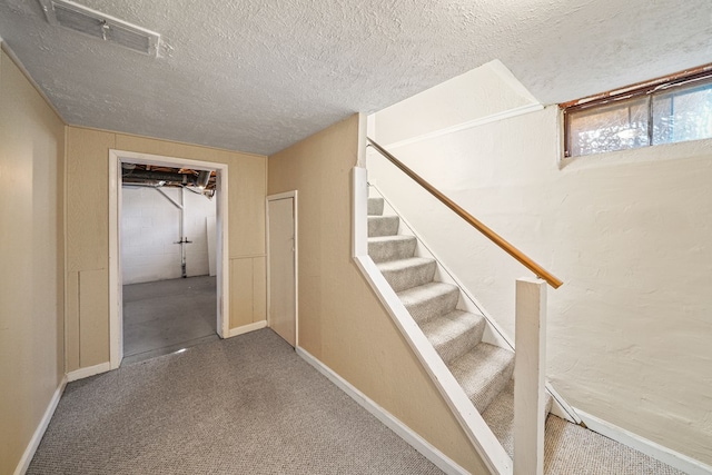 staircase featuring visible vents, a textured ceiling, concrete block wall, carpet flooring, and baseboards