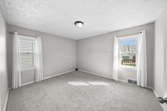 carpeted spare room with baseboards, visible vents, and a textured ceiling