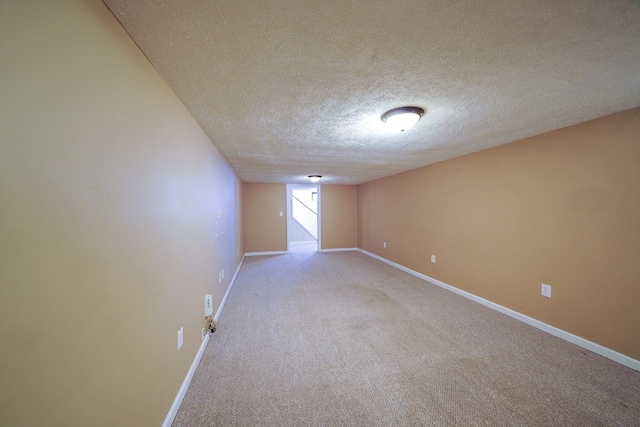 spare room with a textured ceiling, baseboards, and light carpet