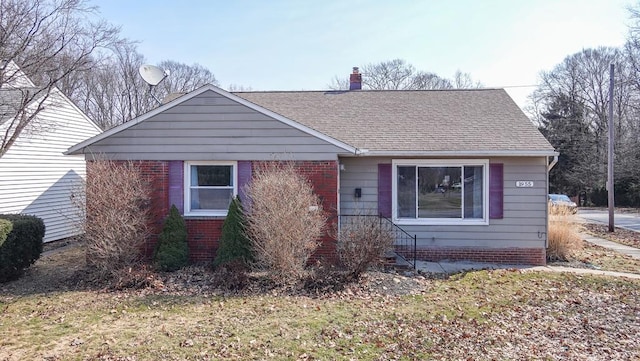 view of front of home with brick siding, roof with shingles, and a chimney