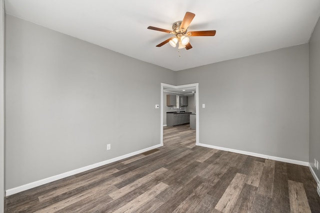 unfurnished room featuring dark wood finished floors, a ceiling fan, and baseboards