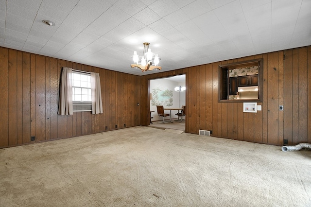 carpeted spare room featuring a notable chandelier and wood walls