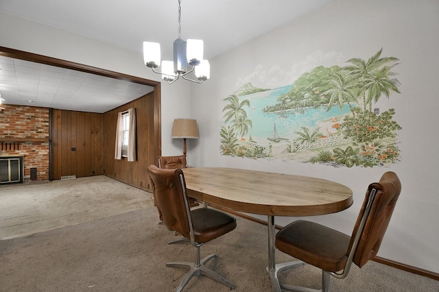 dining room featuring light carpet, a brick fireplace, a notable chandelier, and wooden walls