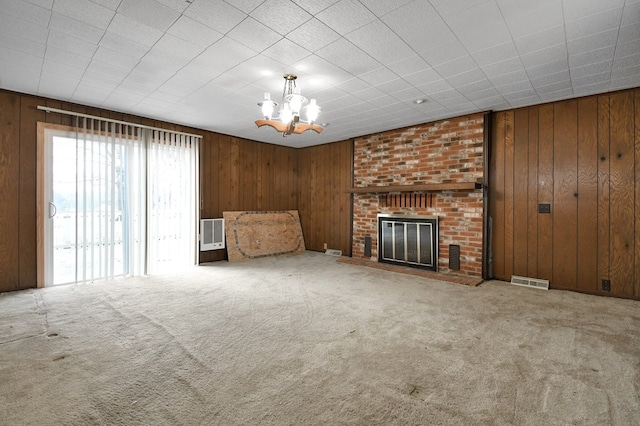 unfurnished living room with wooden walls, a fireplace, carpet flooring, and a notable chandelier