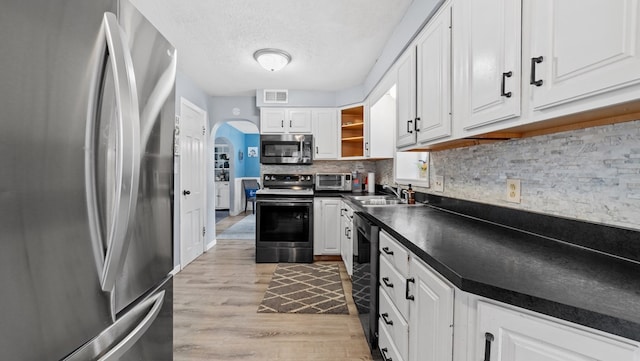 kitchen with white cabinets, appliances with stainless steel finishes, decorative backsplash, sink, and light hardwood / wood-style floors